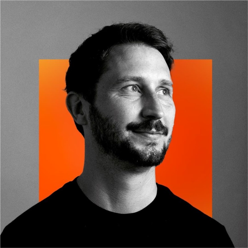 A monochrome portrait of Luke Cope, a young white man, with orange and grey squares in the background.